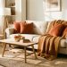 Salon lumineux et chaleureux en automne avec canapé beige, plaids camel, coussins terracotta, tapis épais et mobilier en bois clair baigné par une douce lumière de fin de journée.