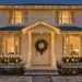 Façade d’une maison chaleureusement décorée pour Noël, avec guirlandes LED blanc chaud, couronne végétale et jardinières illuminées au crépuscule.